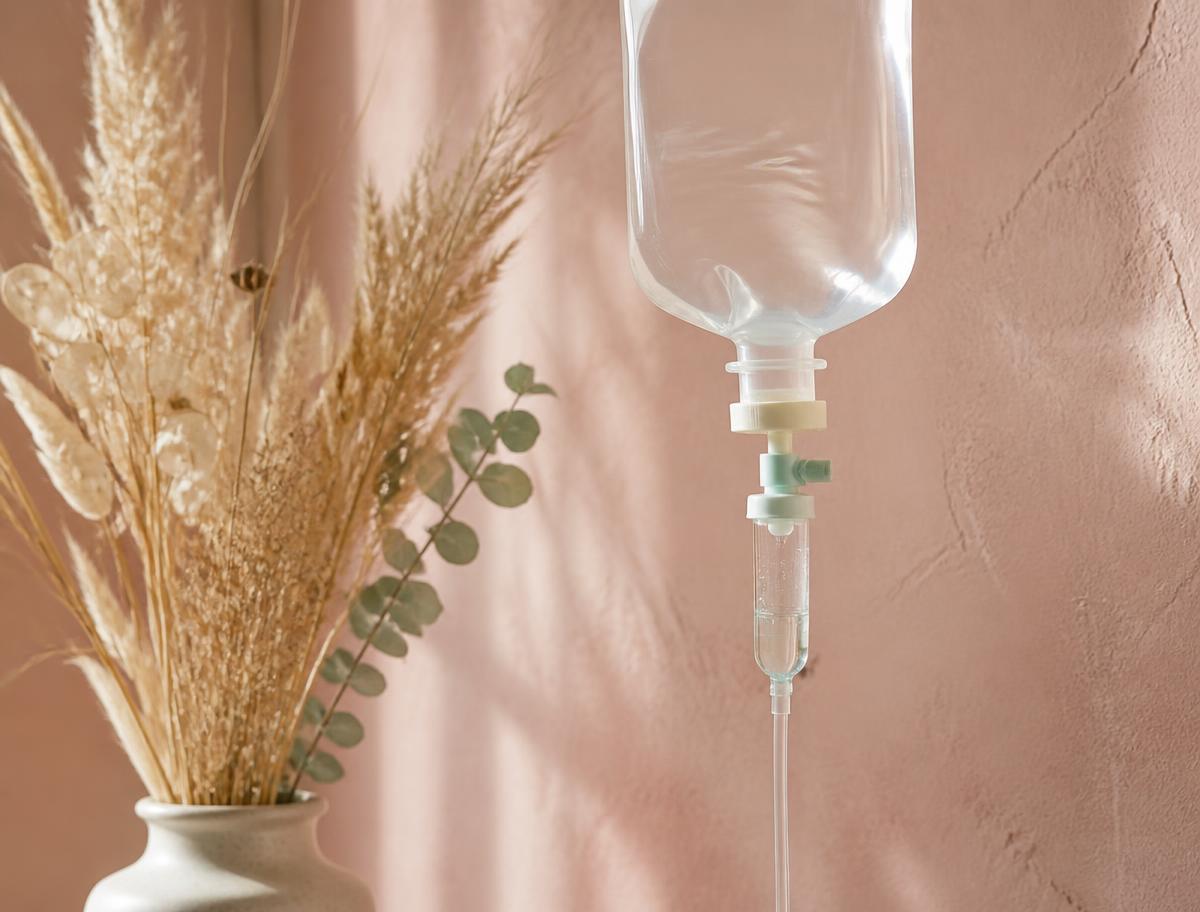 An infusion bag and drip line against a warm blush wall